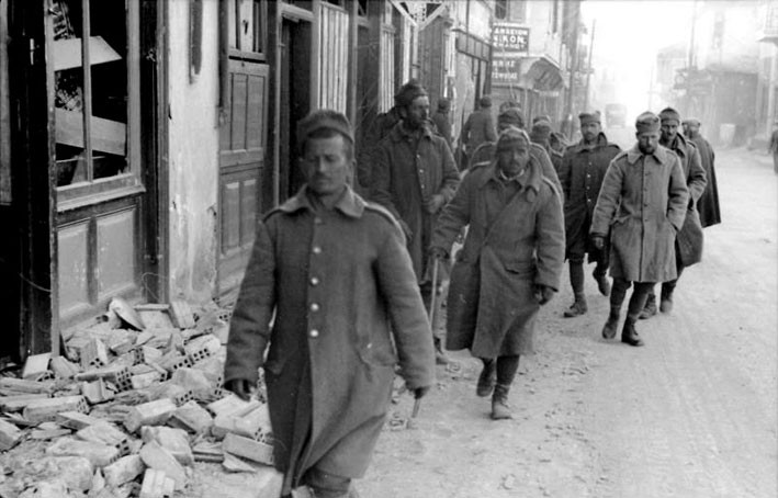 Greek soldiers march through a rubble-filled street