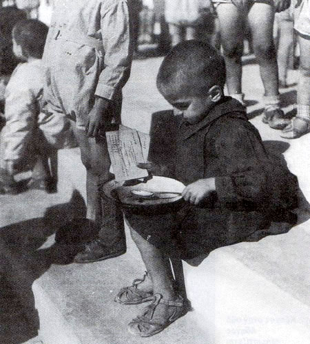 Malnourished child sitting with bowl.